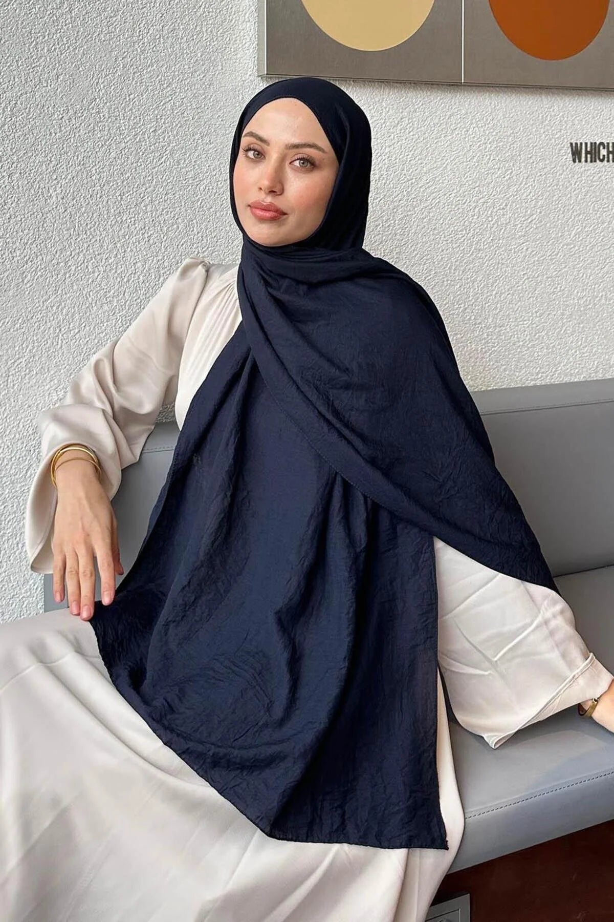 Woman in a navy Comfort Cotton Hijab draped over a cream outfit, seated view