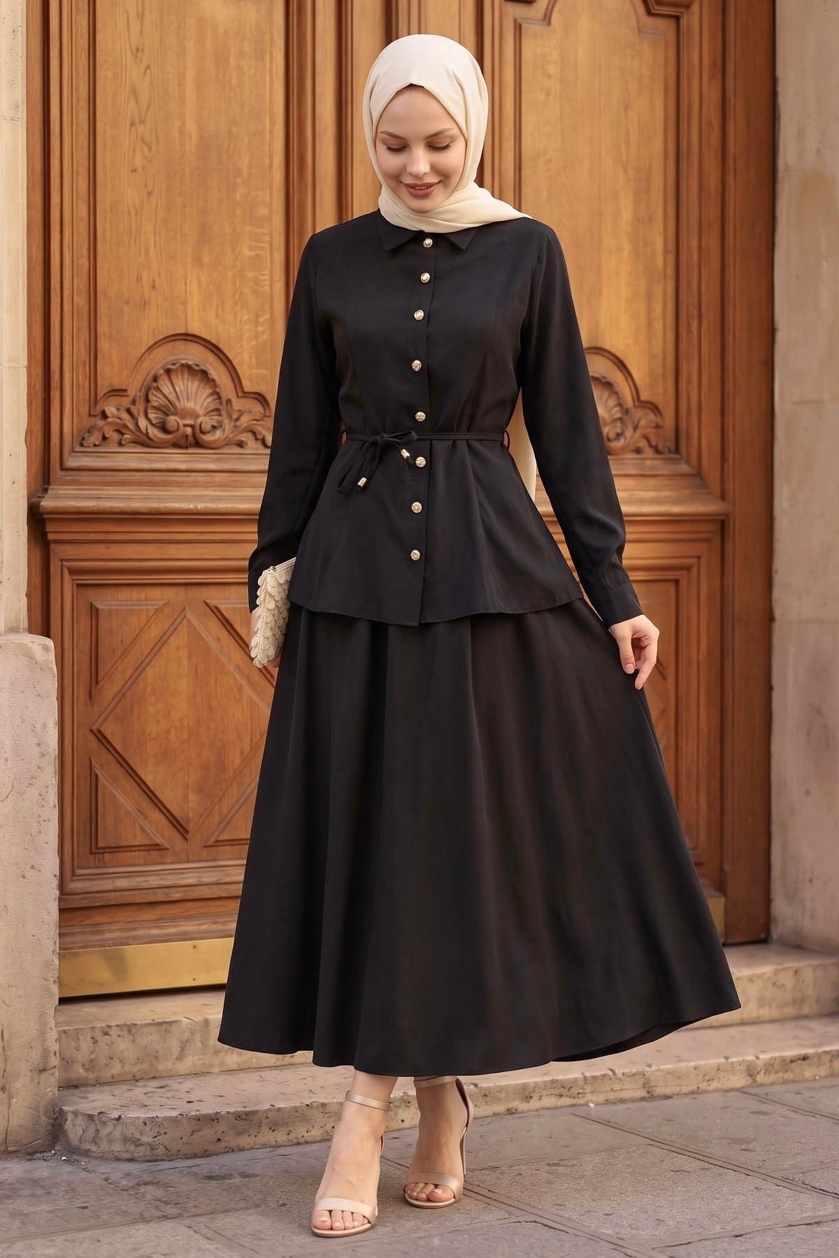 Woman in a hijab wearing the Ayla modest skirt set in black: tie-waist button-front shirt and A-line maxi skirt, front view