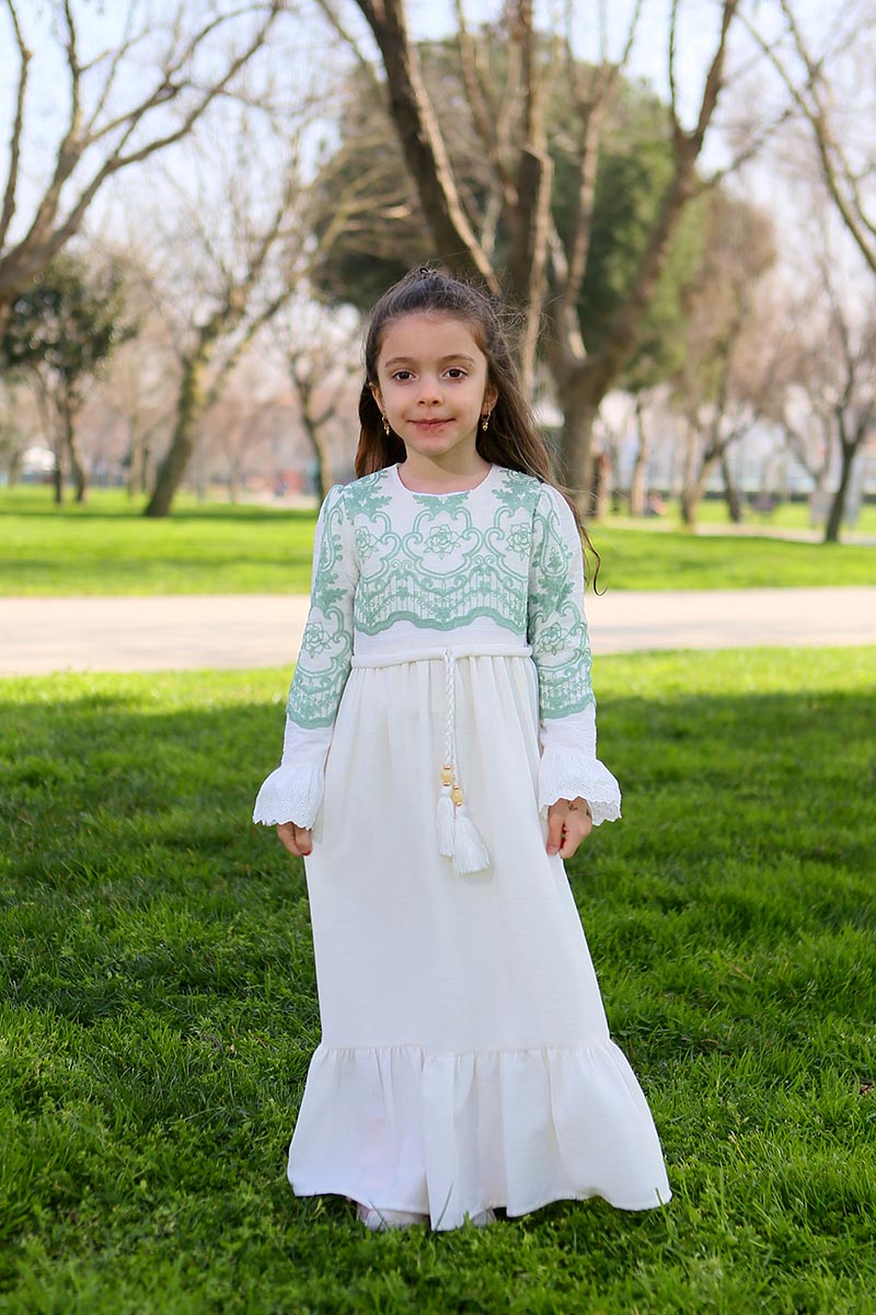 Girl wearing the white linen modest maxi dress with mint floral embroidered bodice, ruffled cuffs and tassel tie waist