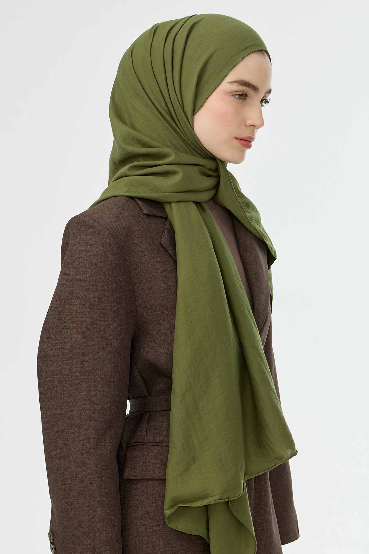 Woman wearing the olive Comfort Cotton Hijab with a brown coat, three-quarter view