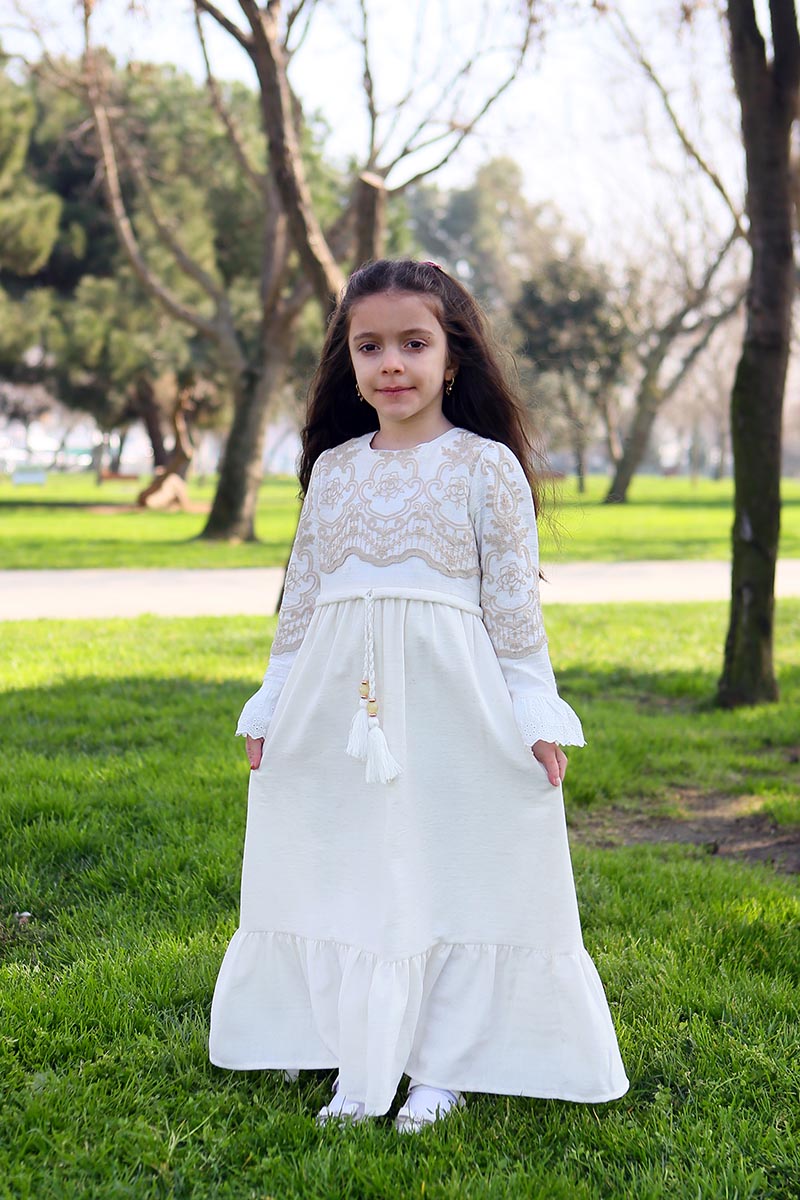 Girl wearing the white linen modest maxi dress with mink floral embroidered bodice, ruffled cuffs and tassel tie waist