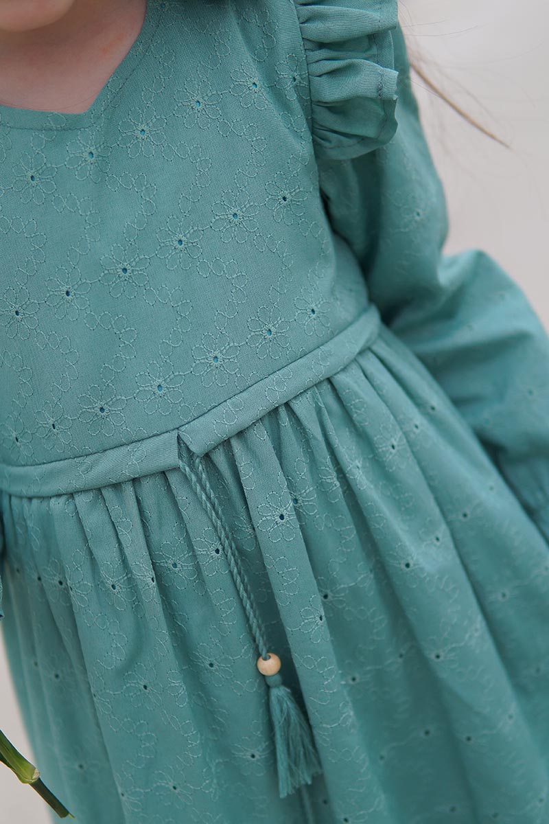 Close-up of the Dahlia girls' modest dress in teal broderie anglaise with ruffled shoulder and tassel tie waist