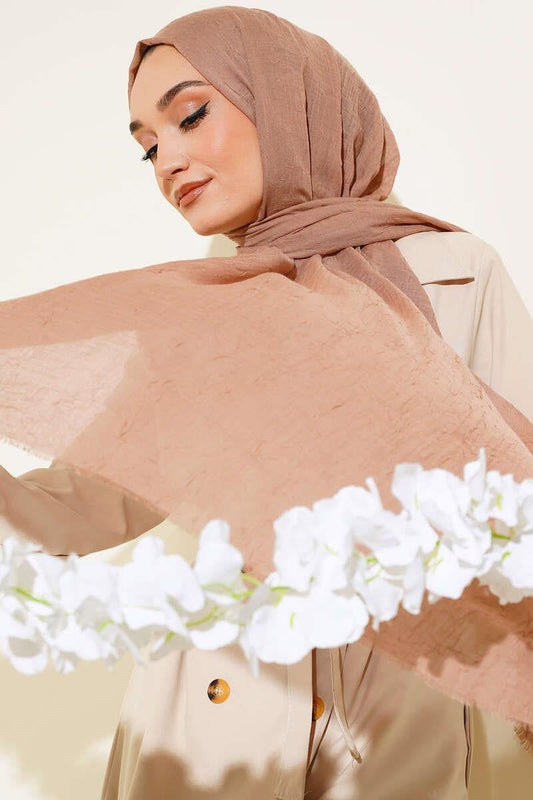 MODESTIQUE Bamboo Crush Hijab in Mink, held open in front of white flowers to show the sheer crinkled fabric.