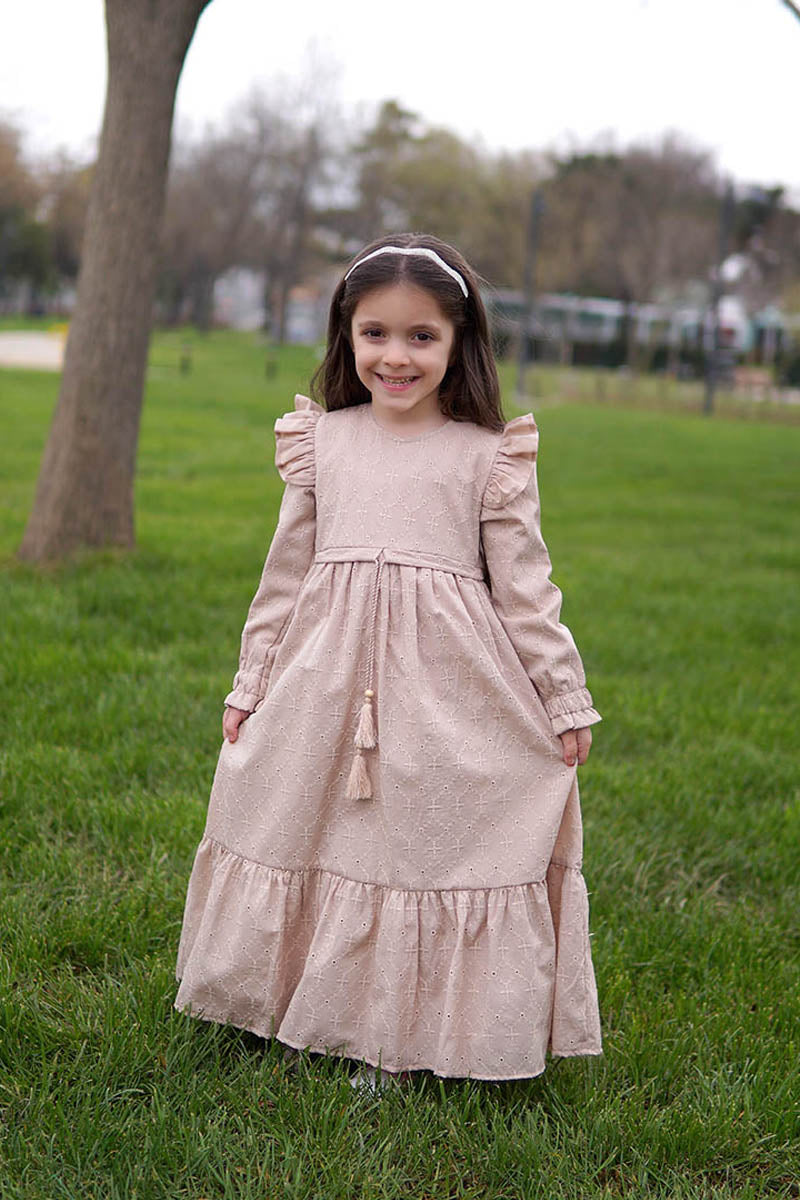 Girl wearing the Dahlia modest maxi dress in mink broderie anglaise with ruffled shoulders and tassel tie, in a park
