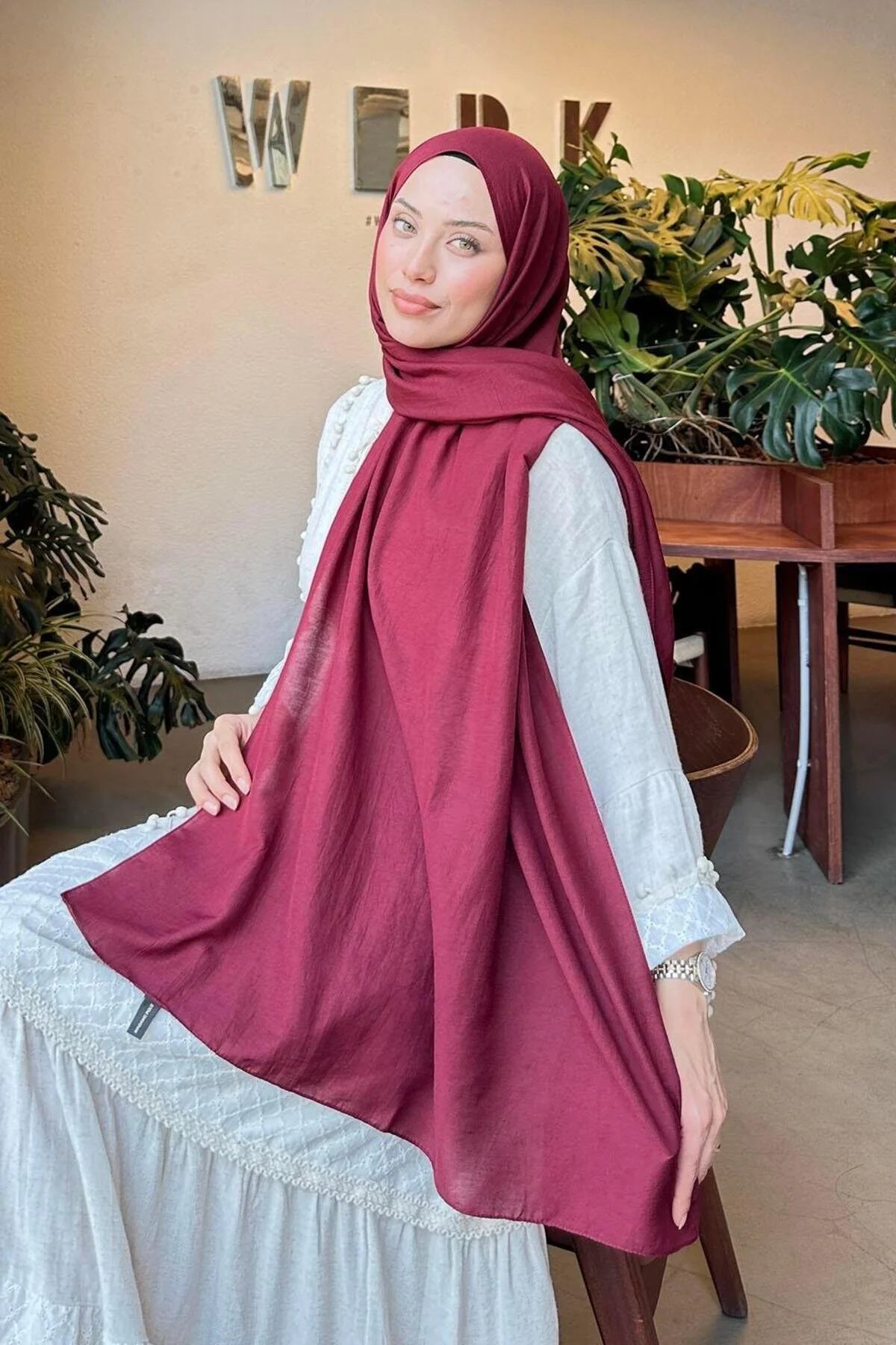 Woman in a maroon Comfort Cotton Hijab draped over a white dress, seated view